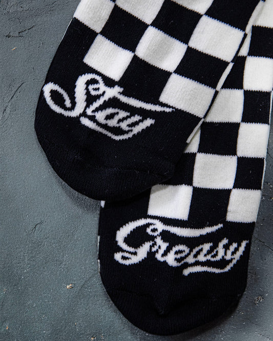Black and white checkered socks with 'Stay Greasy' text on a dark surface