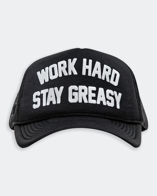 work hard stay greasy black foam trucker hat with white text front view on gray background
