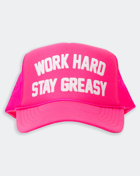 neon pink trucker hat with work hard stay greasy on the front on a grey background