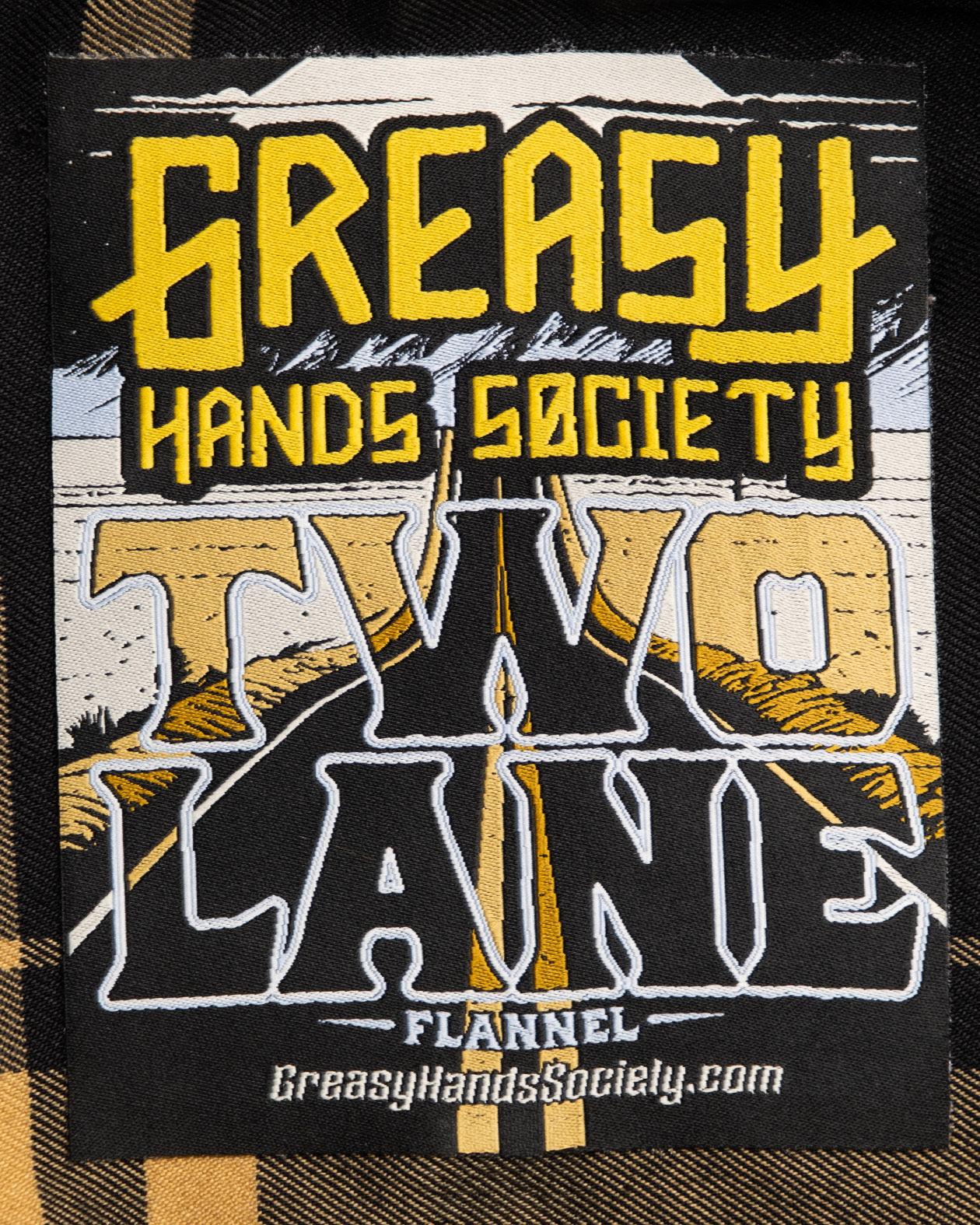 tag label art showing a two-lane highway for the two lane black and gold flannel - The Two-Lane Flannel from Greasy Hands Society