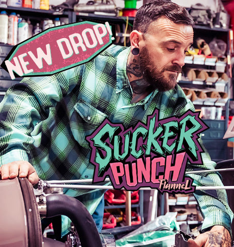Man in plaid shirt with 'Sucker Punch' graphic and 'New Drop' sign in a store setting