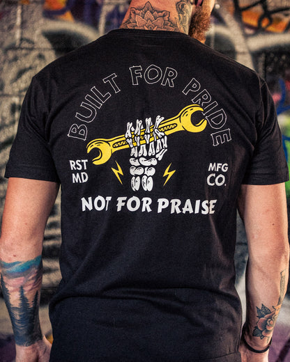 Person wearing a black t-shirt with a graphic design and text on the back, standing in front of a graffiti-covered wall - Built for Pride men's black graphic t-shirt by greasy hands society