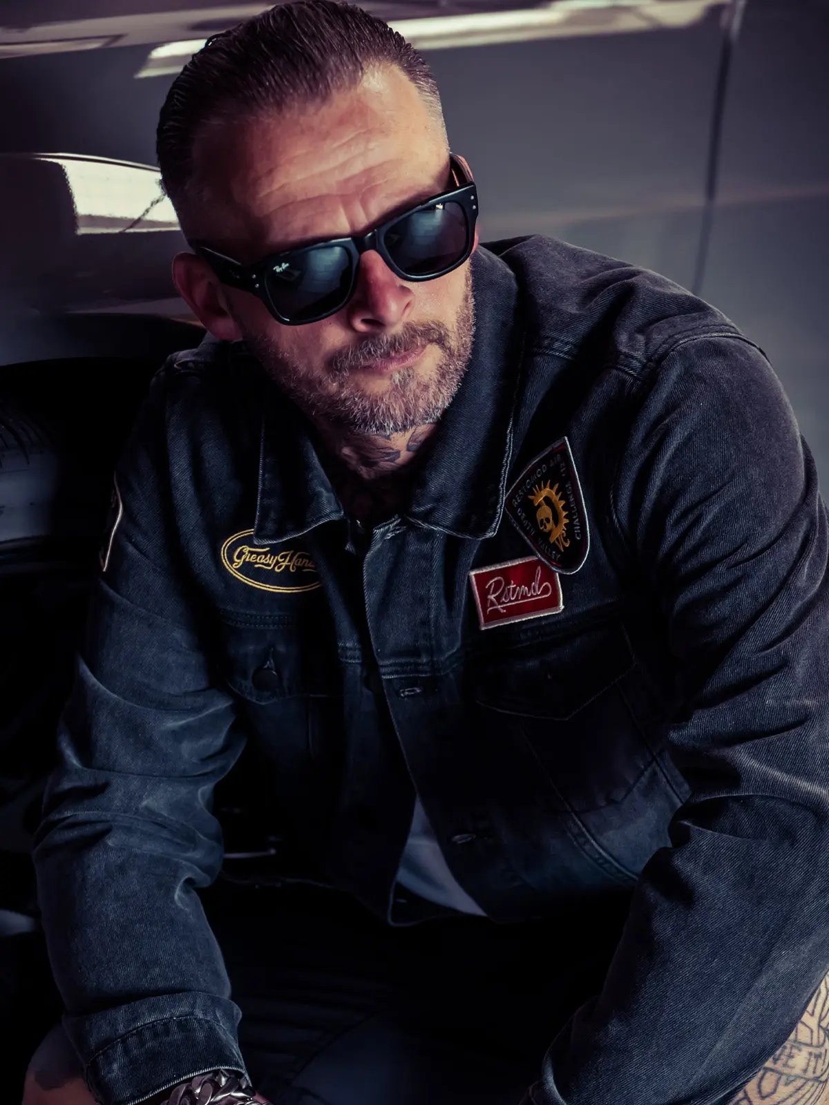 man wearing sunglasses and a denim jacket with patches that say 'RSTMD' 'Greasy Hands Society' and 'Restomod' - The Black Denim Jacket by Greasy Hands Society