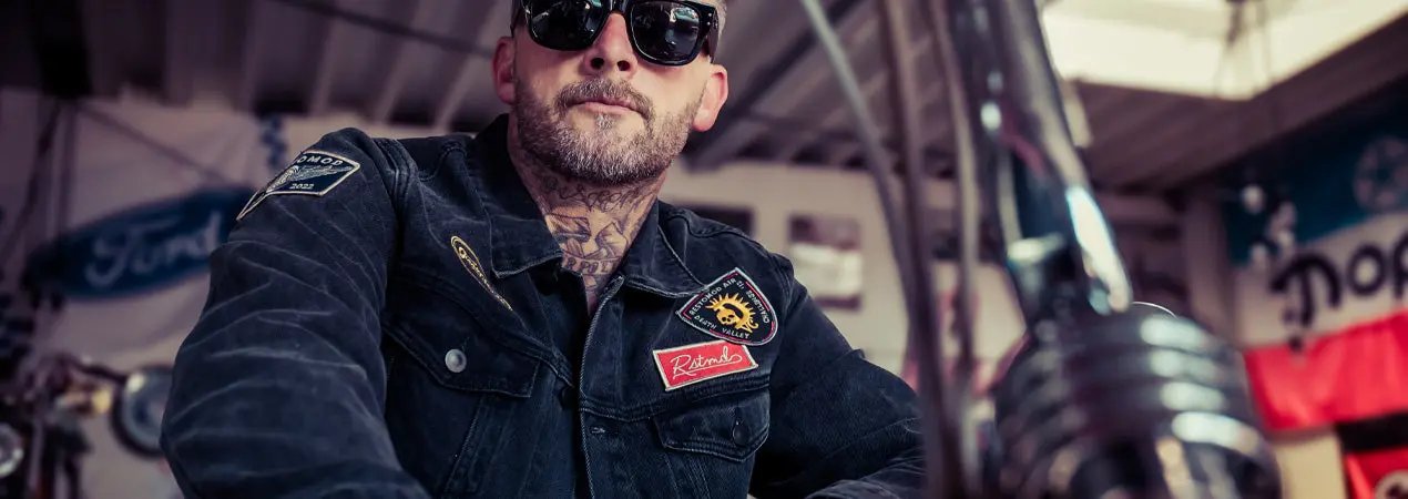 person in an industrial setting wearing unglasses and a black denim jacket - The Black Denim Jacket by Greasy Hands Society