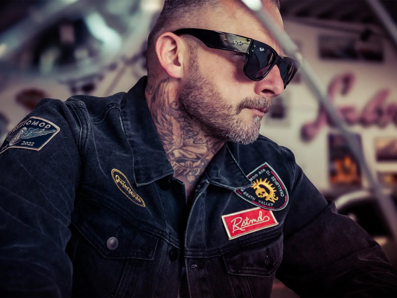 man with tattoos and sunglasses wearing a denim jacket with patches that say 'RSTMD' 'Greasy Hands Society' and 'Restomod' - The Black Denim Jacket by Greasy Hands Society