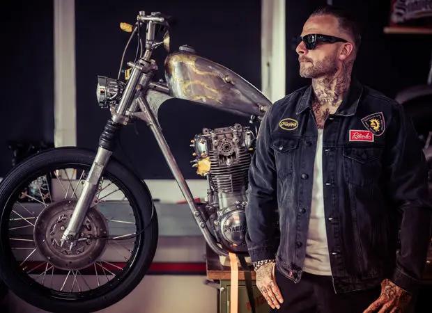 man standing in front of a vintage motorcycle wearing a black denim jacket - The Black Denim Jacket by Greasy Hands Society