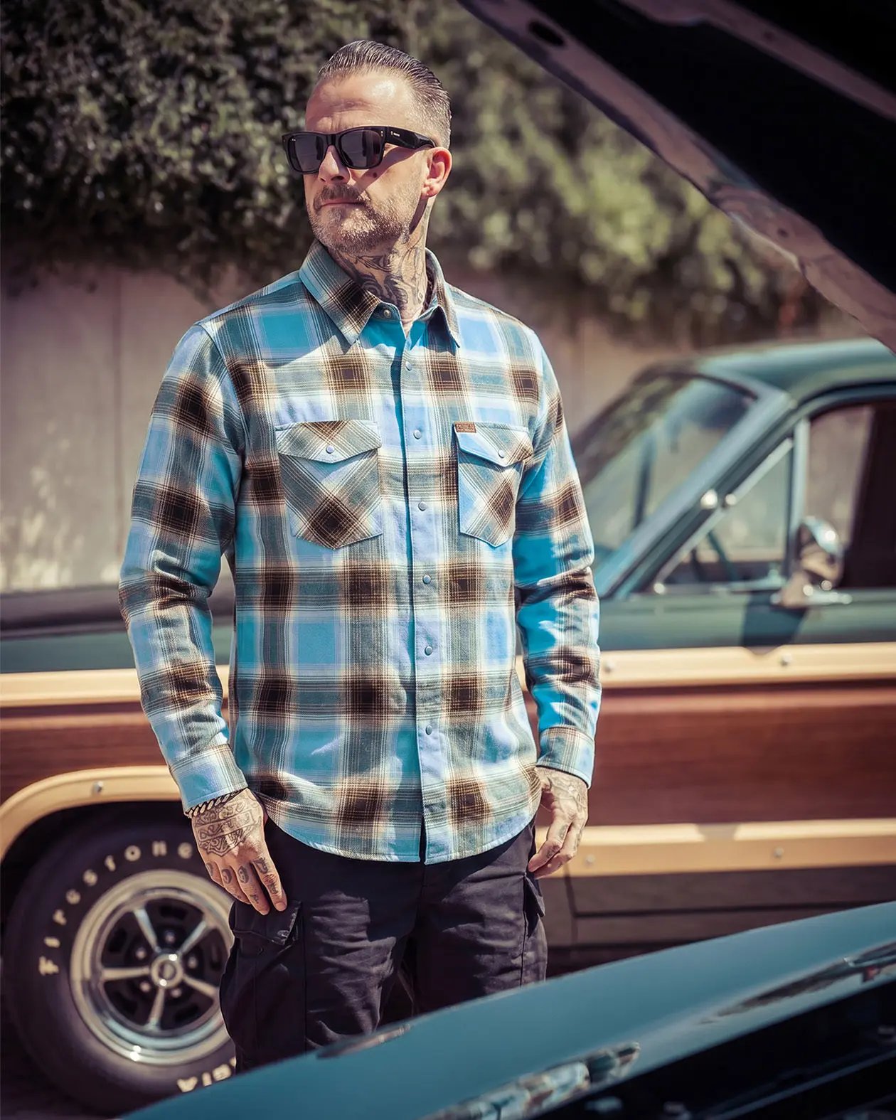 Man wearing a plaid blue and brown flannel shirt and sunglasses standing next to a vintage truck - Cold Start Flannel by Greasy Hands Society