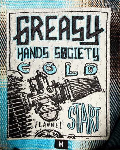 Label with 'Greasy Hands Society' text and graphic design on a textured surface - Cold Start Flannel by Greasy Hands Society