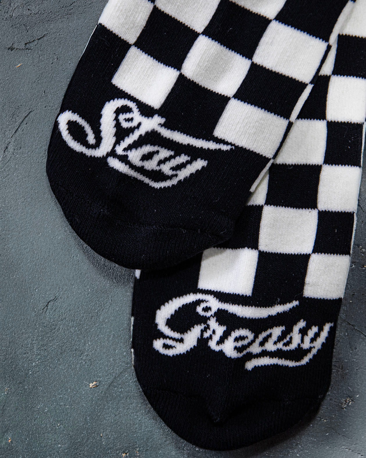 Black and white checkered socks with 'Stay Greasy' text on a dark surface
