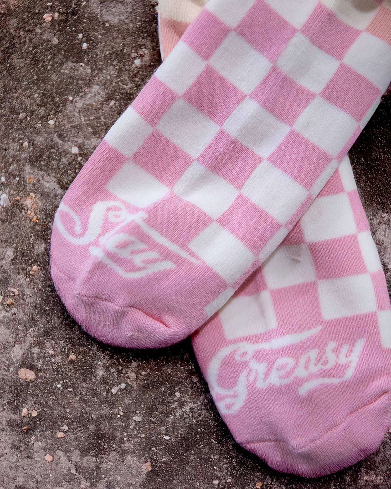 Pink and white checkered socks with 'Stay Greasy' text on a concrete surface