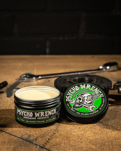 an open containers of Psycho Wrench grooming pomade on a wooden surface with tools in the background - Psycho Wrench OIL & GRIT Pomade by Greasy Hands Society