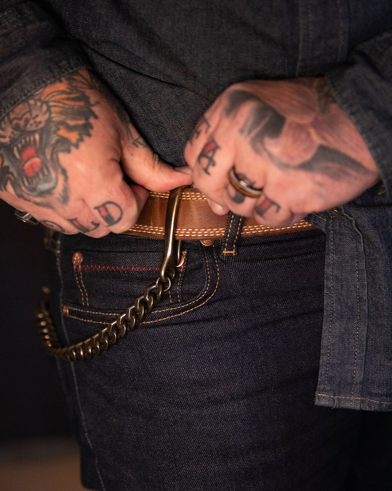 Person with tattoos adjusting a brown belt with a gold buckle.