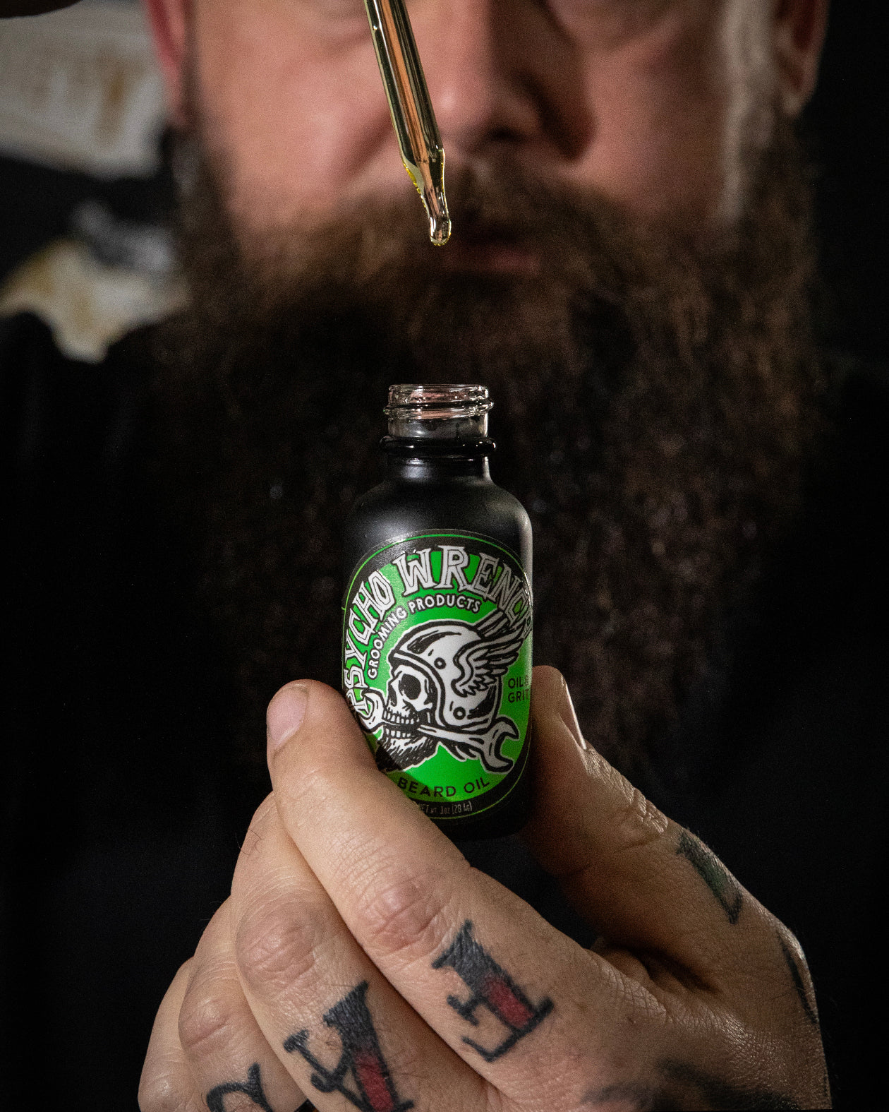 Person holding a bottle labeled 'Psych Wrench gooming products beard oil' with a dropper close to the bottle.