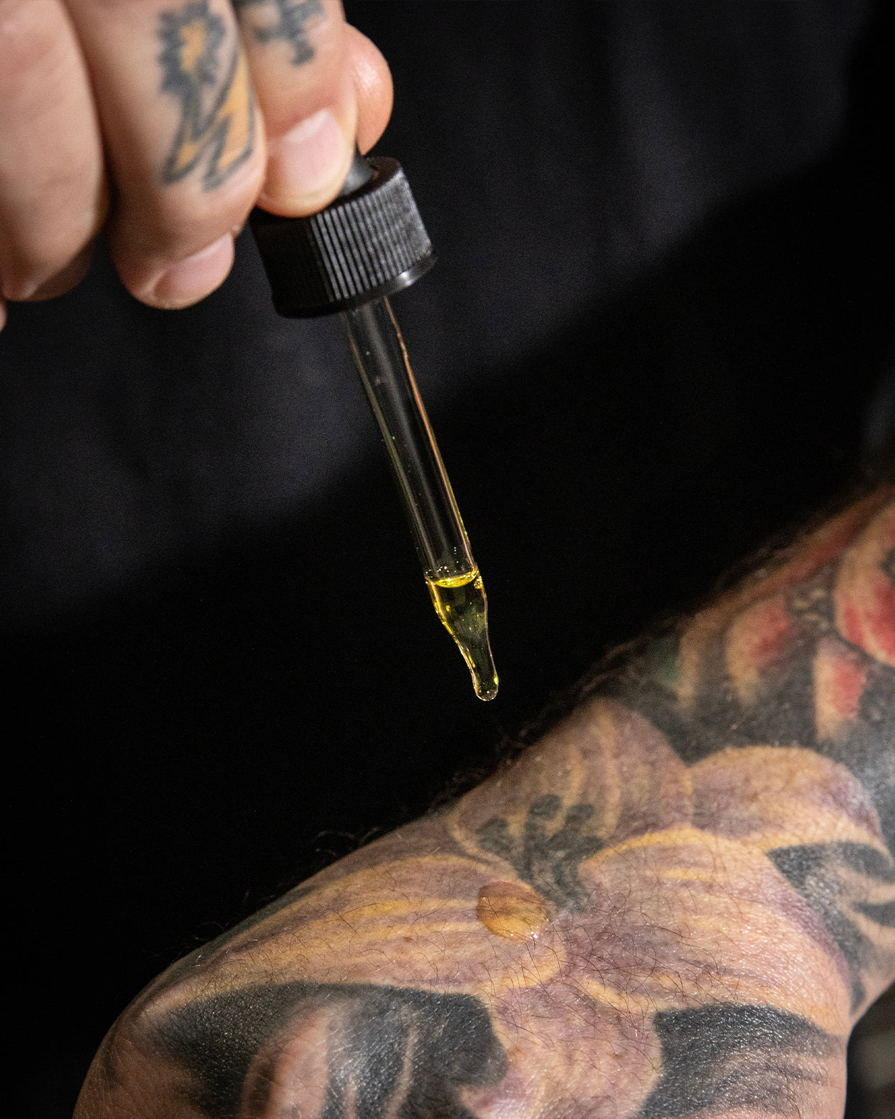 Dropper with a small amount of liquid held above a tattooed arm - Psycho Wrench Tattoo Oil -Oil & Grit Scent by Greasy Hands Society
