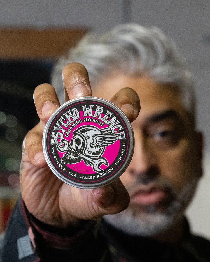 Person holding a container of Psycho Wrench grooming product with smooth idle scent with a blurred background