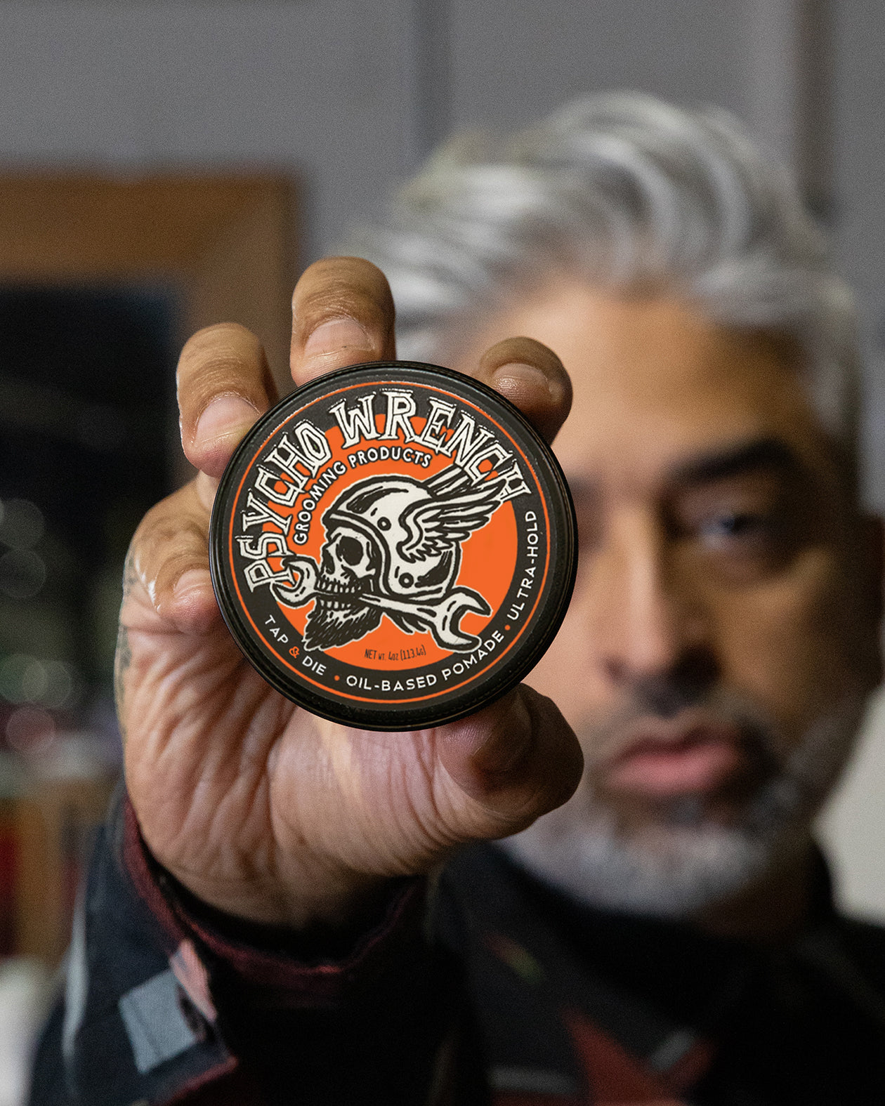 Person holding a 'Psycho Wrench' pomade container with a blurred background - Psycho Wrench Tap & Die Pomade by Greasy Hands Society
