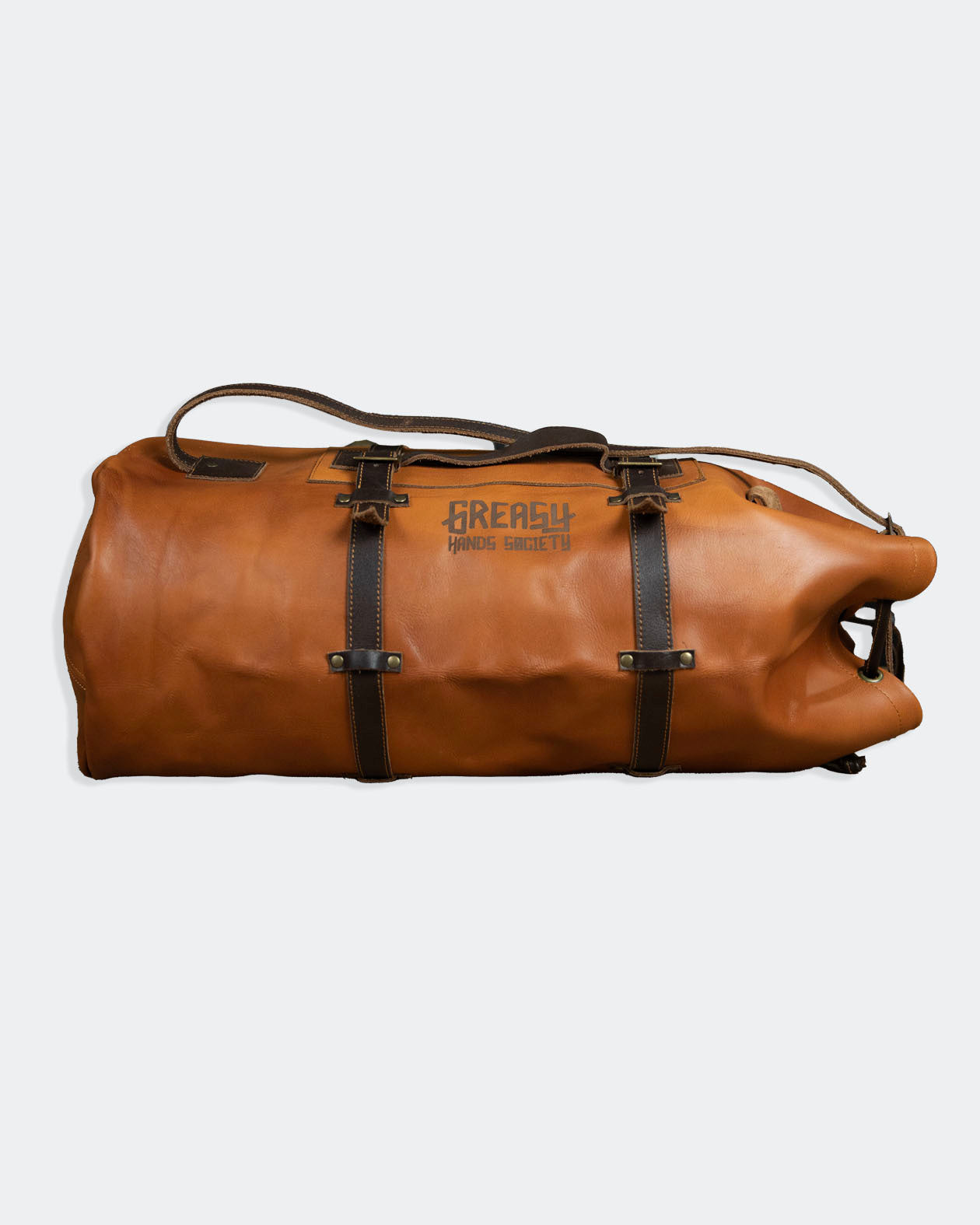 Brown leather duffel bag for men with dark brown straps on a gray background - The Freeloader Duffel Bag from greasy hands society
