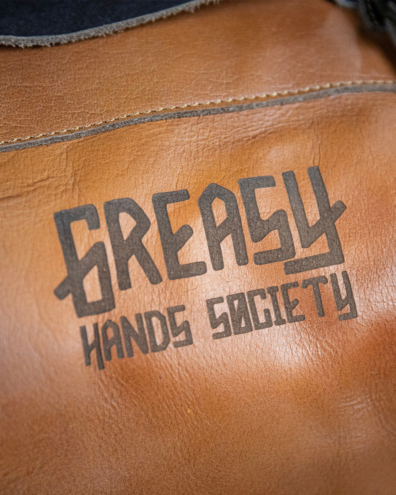 detail of the greasy hands society logo on the brown leather duffel bag - The Freeloader Duffel Bag from greasy hands society