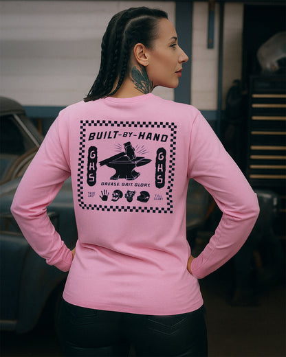 woman wearing a pink long-sleeve shirt with a graphic design on the back, standing in a garage.