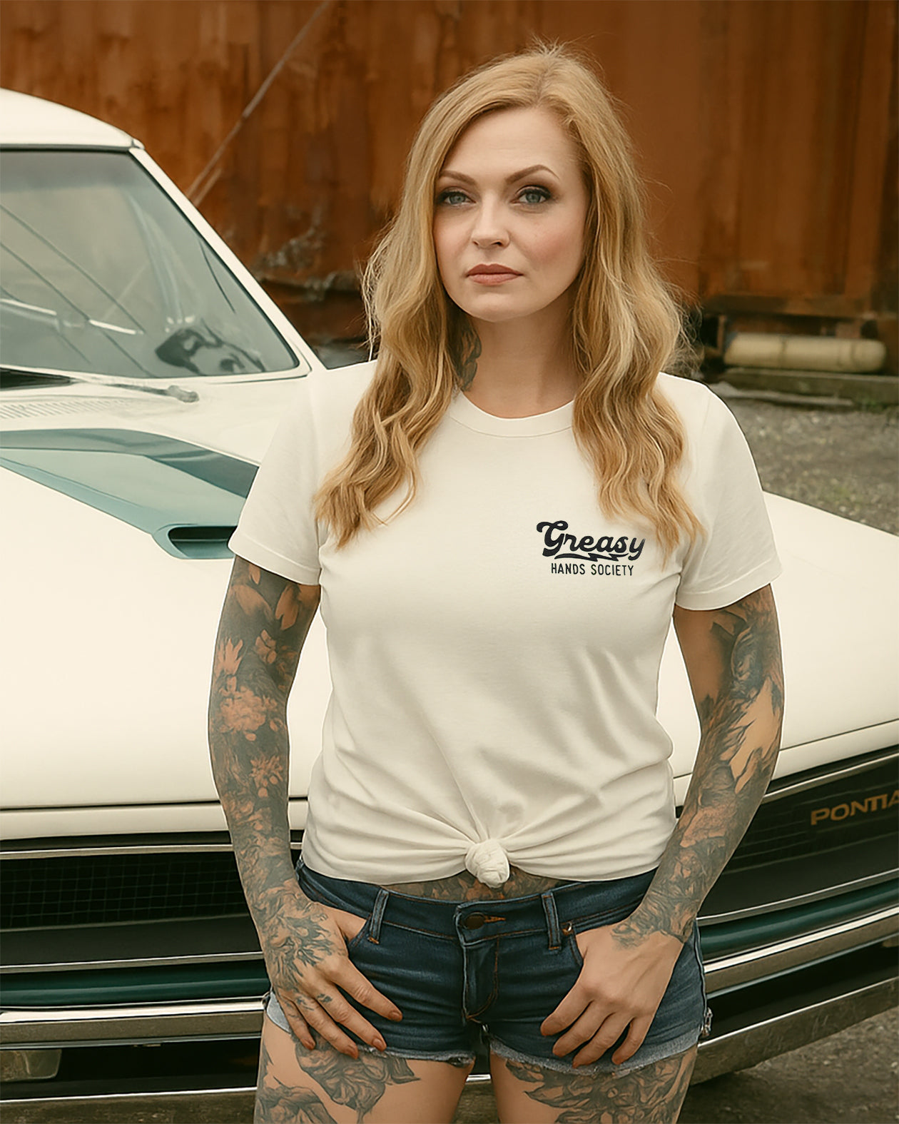 womens' destination graphic tee in vintage white - Woman wearing a white t-shirt with 'Greasy Hands Society' text in front of a vintage car.