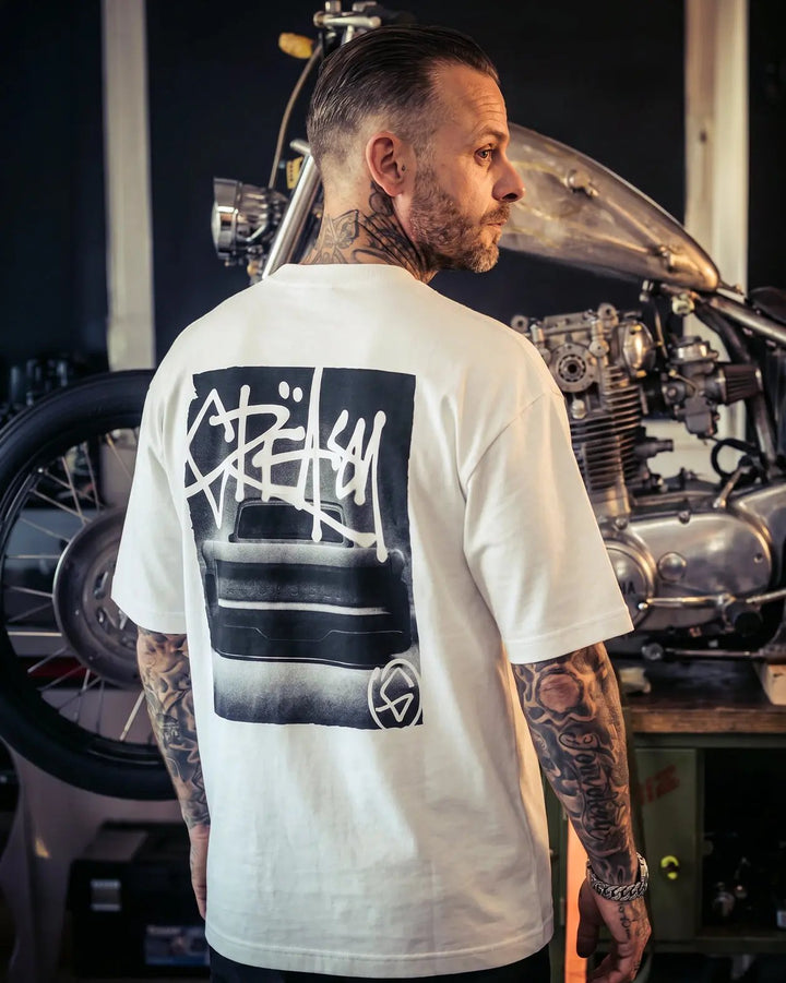 Person wearing a white t-shirt with a graphic design in a workshop setting - Tailgate Boxy White Heavyweight graphic Tee by Greasy Hands Society