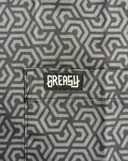 Close-up of a gray and black geometric patterned fabric with a black patch featuring the white 'GREASY' brand logo on the pocket - The Burnout Button-Up Shirt by Greasy Hands Society