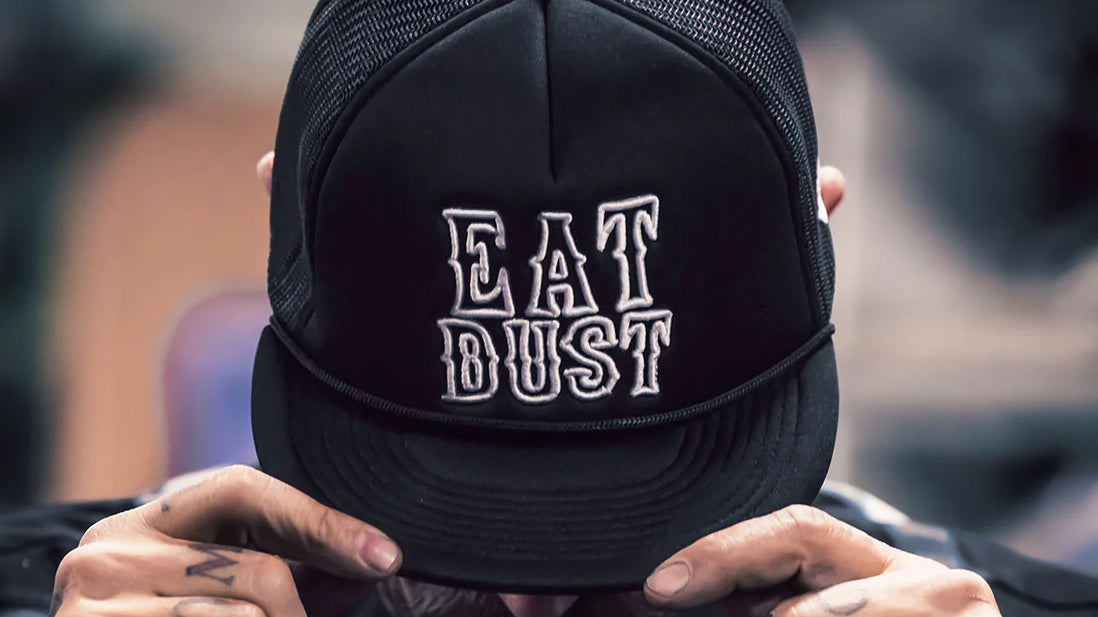 Black cap with 'EAT DUST' text held by a person against a blurred background
