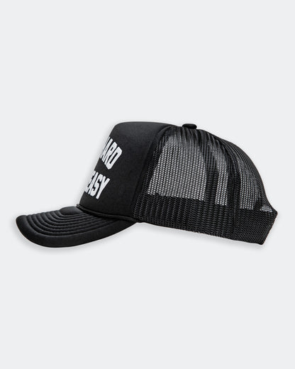 work hard stay greasy black  foam trucker hat with white text side view on a gray background