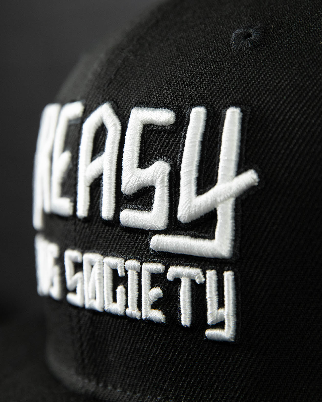 detail shot of a black cap with white greasy hands society logo on the front - showing the stitching