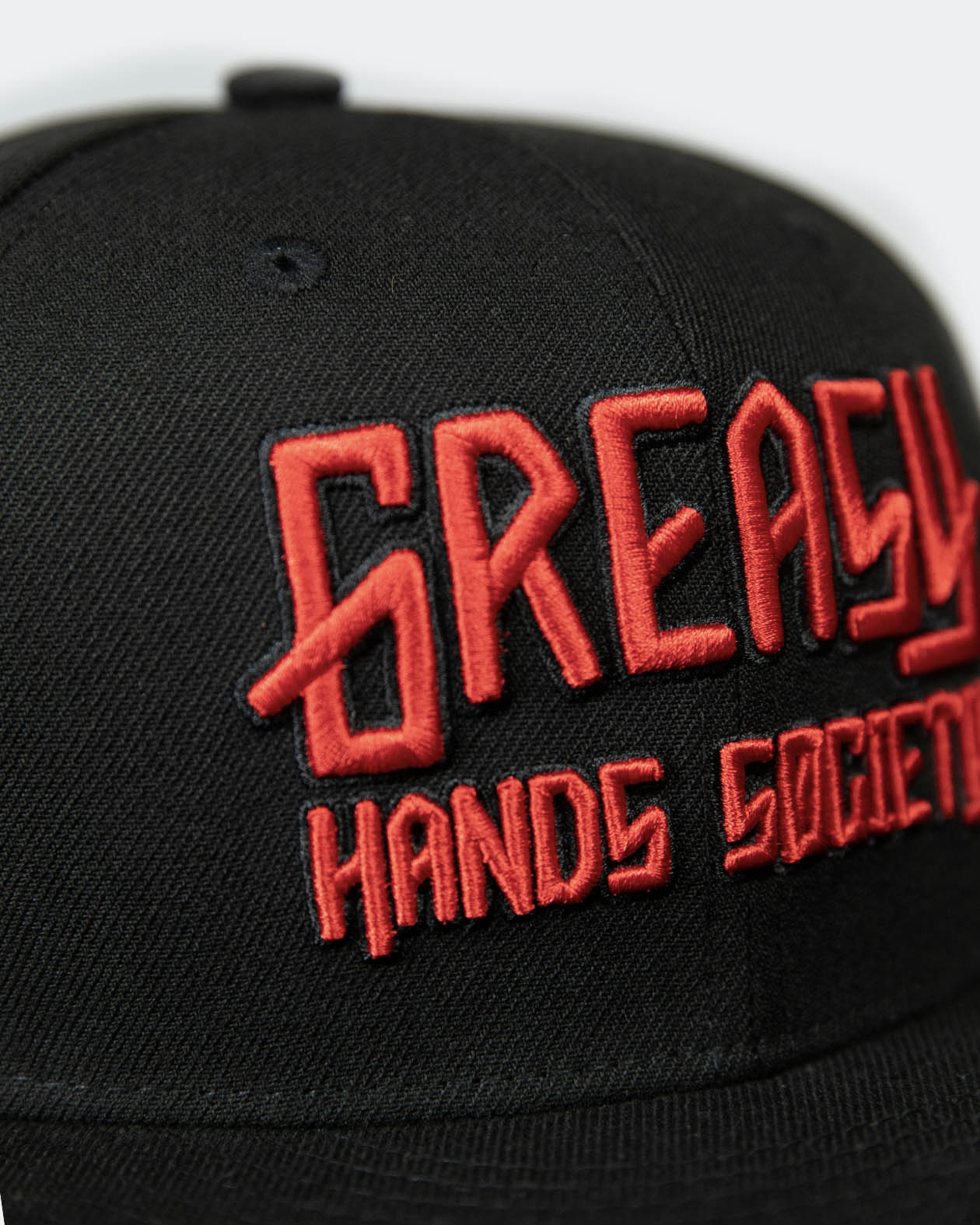 detail shot of a black cap with red greasy hands society logo on the front - showing the stitching