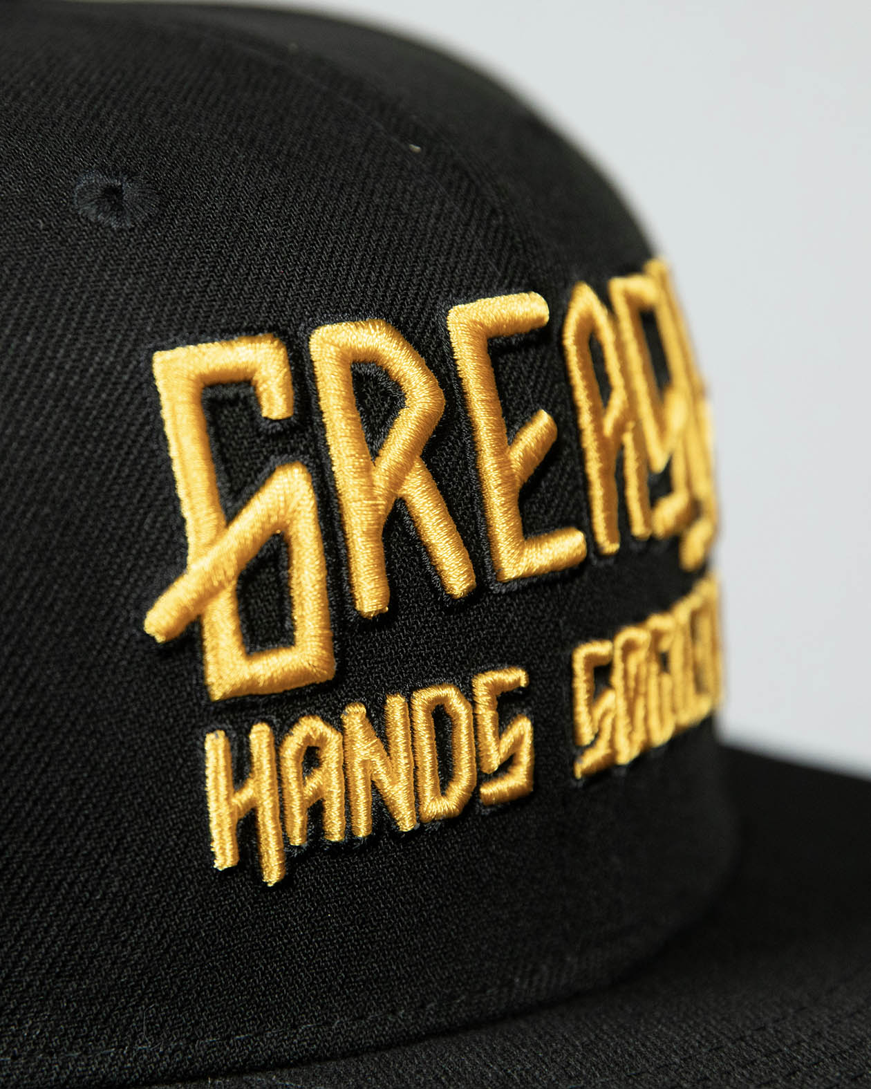 detail shot of a black cap with gold greasy hands society logo on the front - showing the stitching