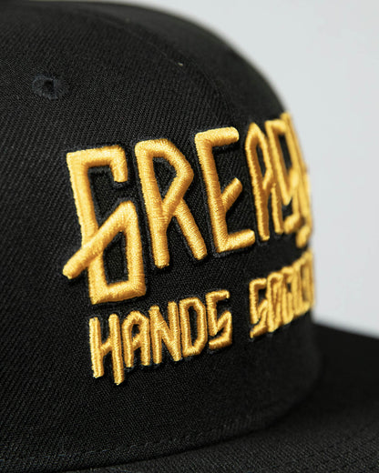 detail shot of a black cap with gold greasy hands society logo on the front - showing the stitching