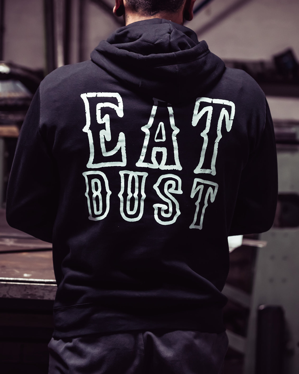Person wearing a black hoodie with 'EAT DUST' text on the back, standing in an indoor setting - Eat Dust Hoodie by Greasy Hands Society