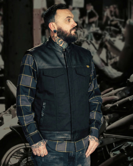 man wearing a black leather and canvas vest with a black and gray flannel - the vest is called the jacinto leather vest
