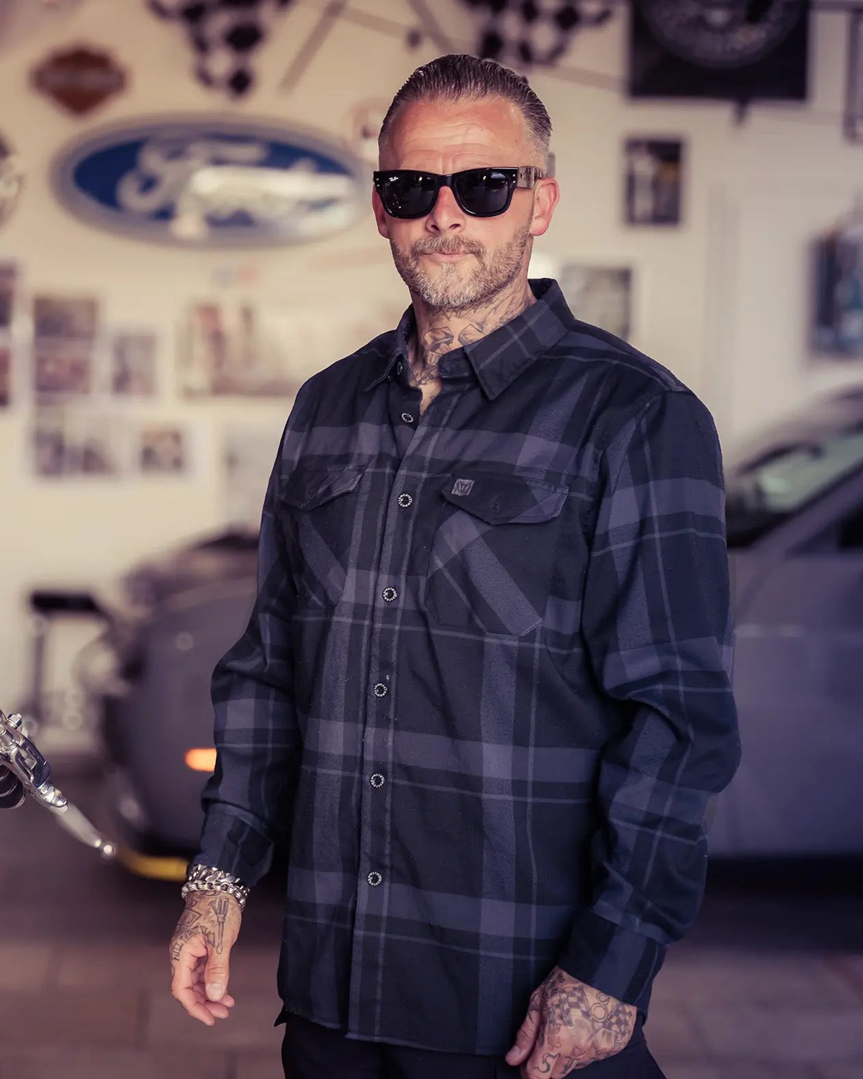 Man wearing sunglasses and a plaid black flannel shirt in a garage setting - the Synister Black Continental Flannel by Greasy Hands Society