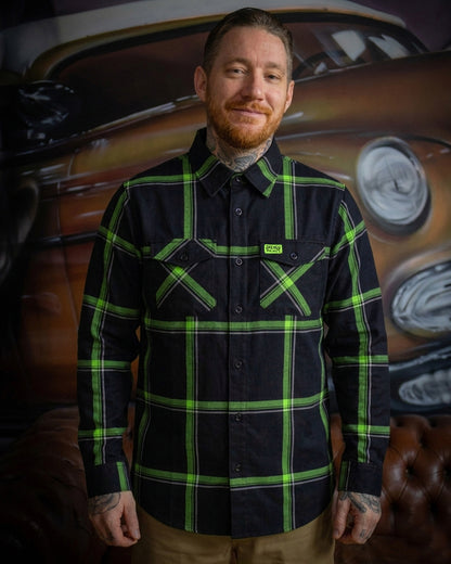 Man wearing a black and green plaid flannel shirt with a vintage car in the background - The Moto Flannel by Greasy Hands Society