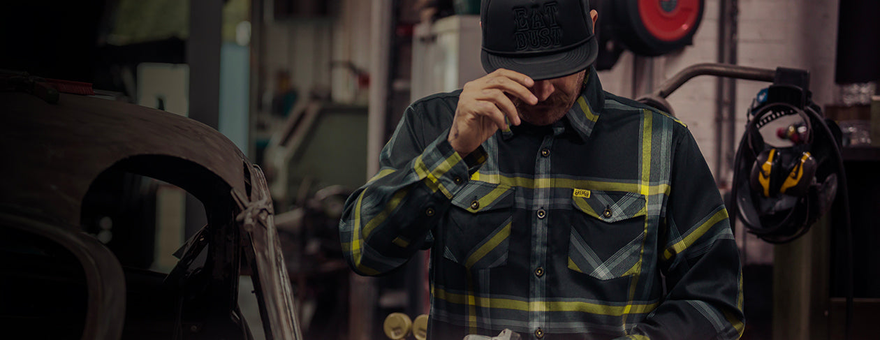 man wearing the eayt dust black and yellow flannel - plaid flannel shirt and cap in a workshop setting