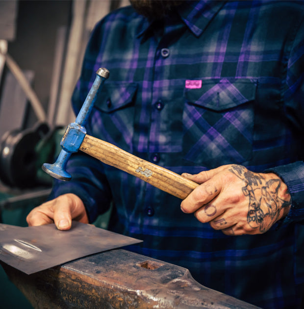 Person working with a hammer on a metal surface, wearing a plaid shirt - Kiss the Sky Flannel by Greasy Hands Society