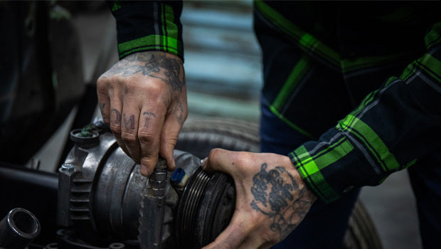 Person working on a mechanical component with tattoos on their hands - The Moto Flannel by Greasy Hands Society