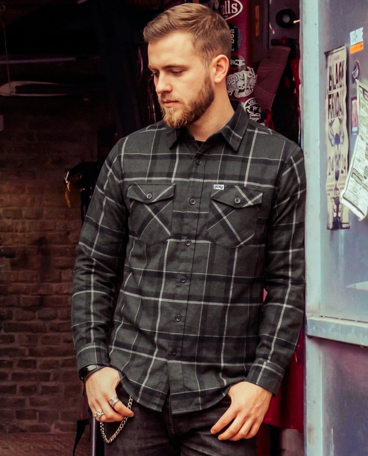Man wearing a plaid gray flannel shirt in an indoor industrial setting - The Dapper Flannel by Greasy Hands Society