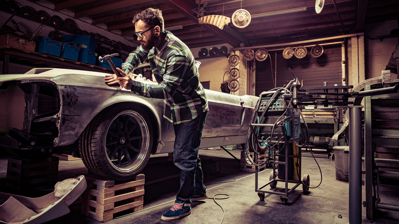 pinstriper blue , pink and yellow flannel worn by a guy working on his car with a hammer