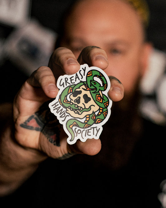 A person holding a sticker with a graphic of a snake and a skull, and the text 'GREAT HANDS SOCIETY'.