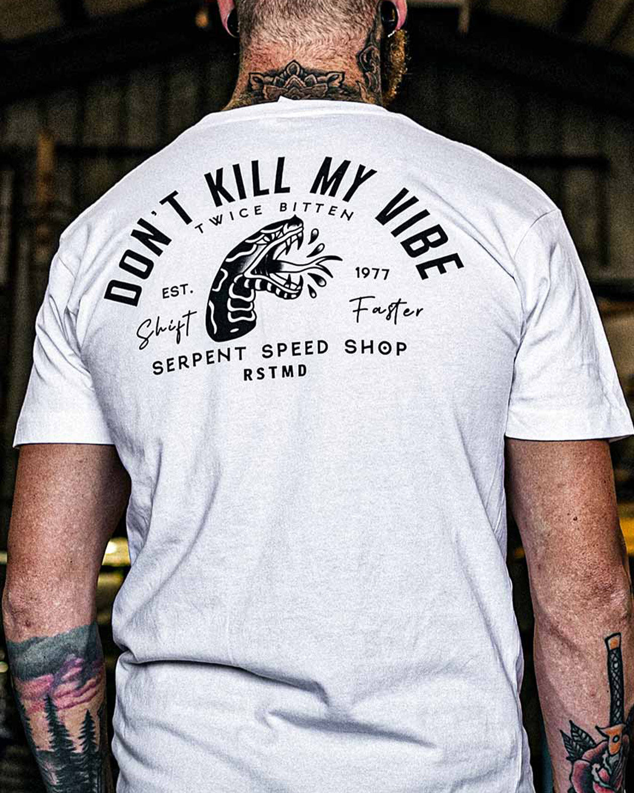 Person wearing a white t-shirt with black text and graphics on the back, set against a blurred indoor background - Don't Kill my Vibe Men's white graphic tee by Greasy Hands Society