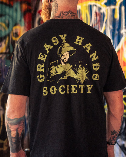 Person wearing a black t-shirt with 'Greasy Hands Society' welding graphic design on the back, standing in front of a colorful mural - Weld On Graphic tee by Greasy Hands Society