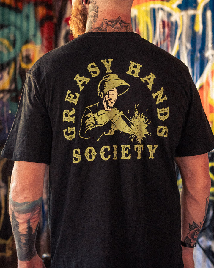 Person wearing a black t-shirt with 'Greasy Hands Society' welding graphic design on the back, standing in front of a colorful mural - Weld On Graphic tee by Greasy Hands Society