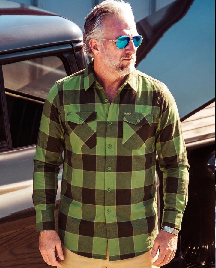 Man wearing a green and brown checkered flannel shirt standing next to a boat - The Griswold Flannel from Greasy Hands Society