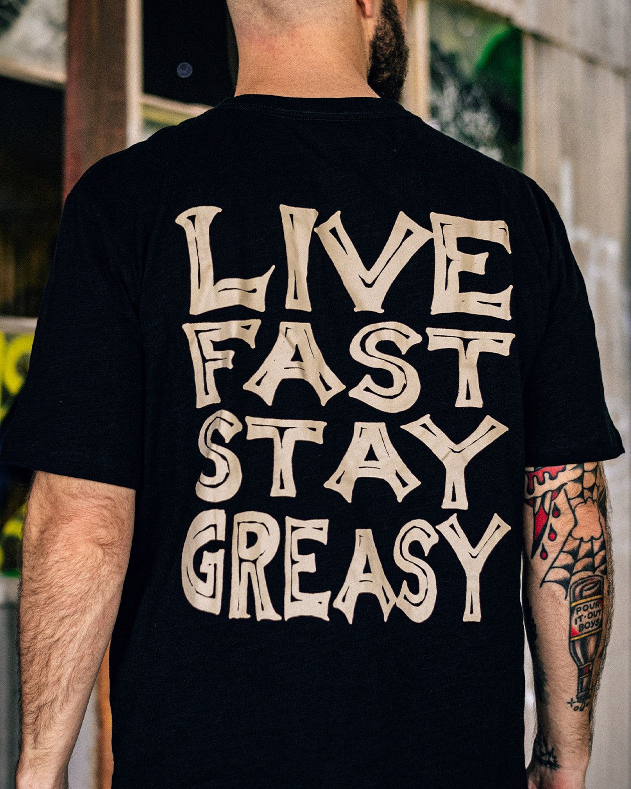 Person wearing a black t-shirt with 'Live Fast Stay Greasy' text on the back - Live Fast Graphic Tee from Greasy Hands Society