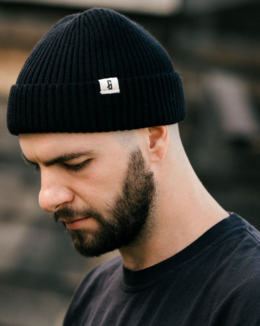 black watch cap with greasy hands society icon 'G' on the tag being worn by a model